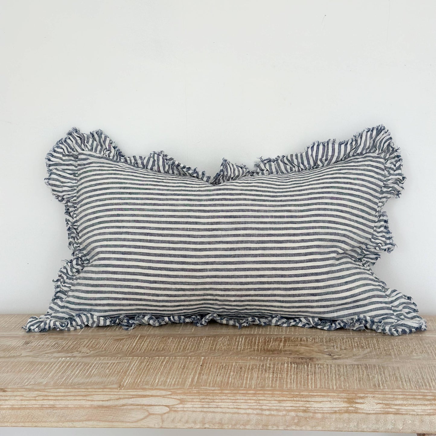 Striped pillow with ruffled edges on a wooden surface against a white background
