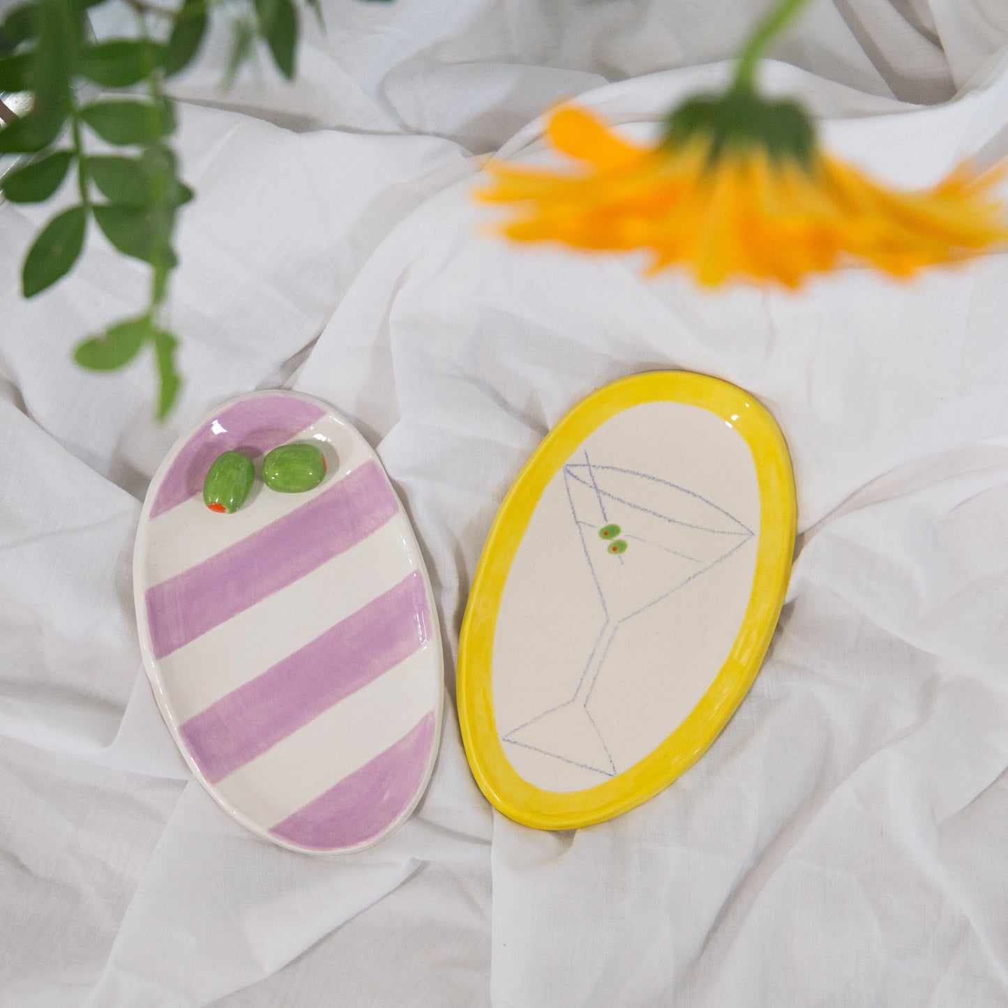 Two ceramic oval plates with decorative designs on a white fabric background.