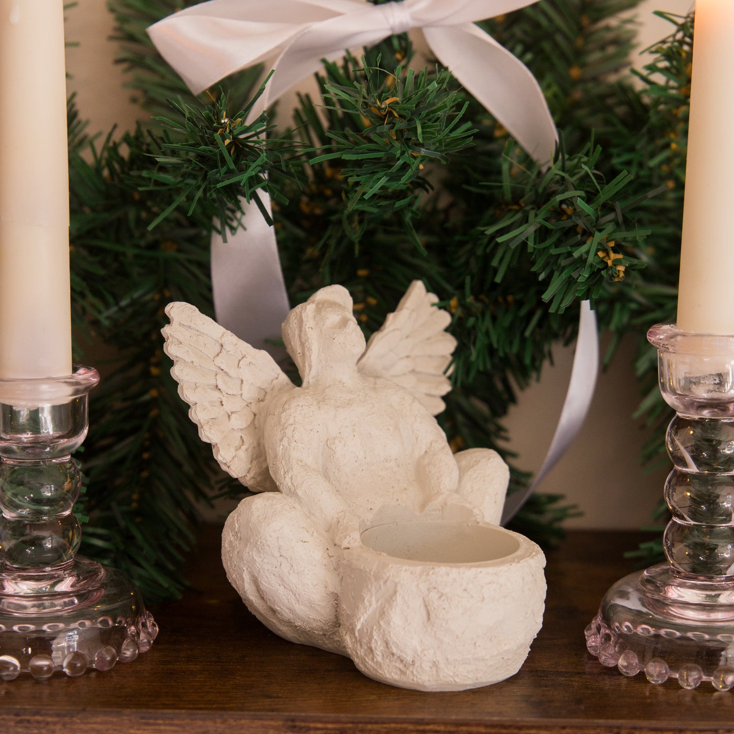 Decorative angel figurine with a candle holder in front of a Christmas tree.