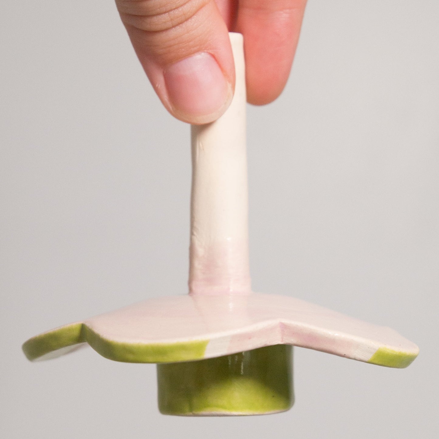 Hand holding a small ceramic or porcelain object with a green base on a plain background