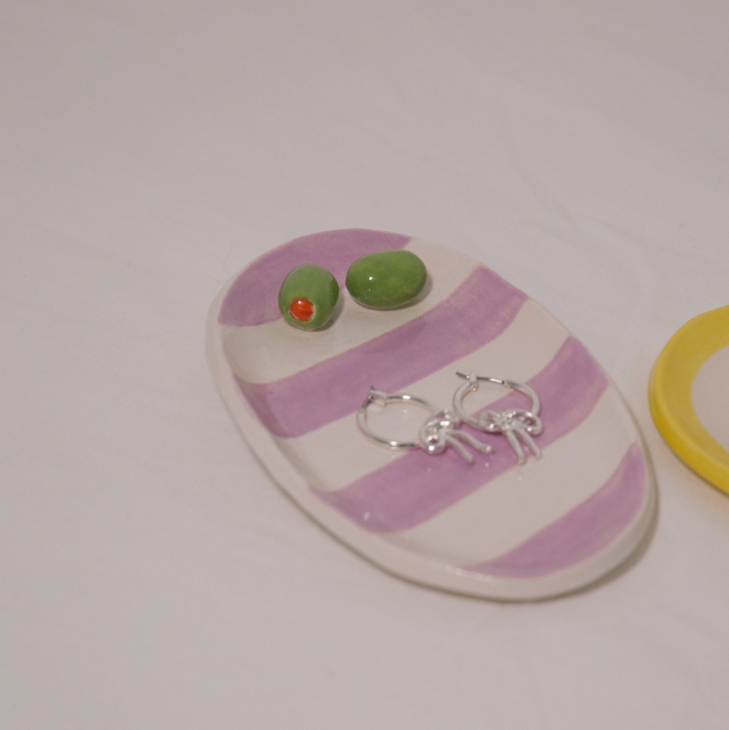 Striped pink and white ceramic dish with green and red earrings on a white background