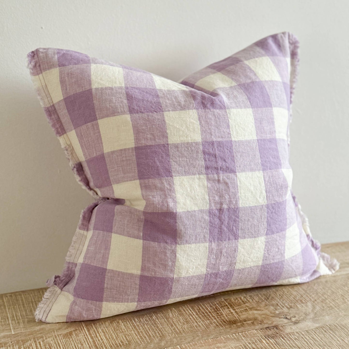 Purple and white checkered pillow on a wooden surface with a neutral background