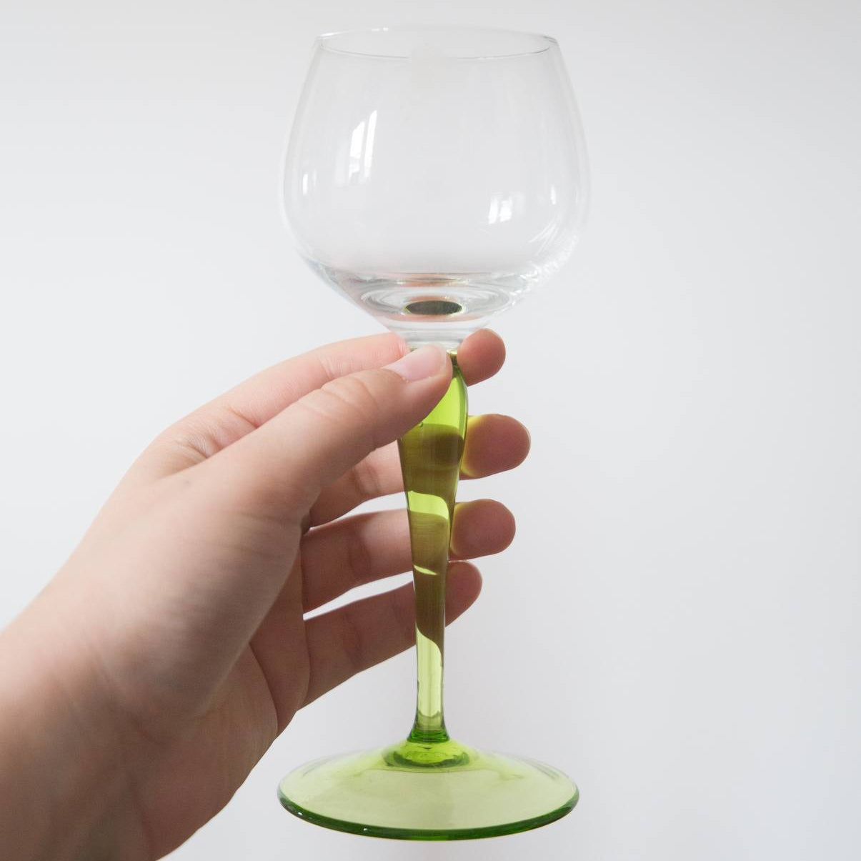 Hand holding a wine glass with a green stem against a white background