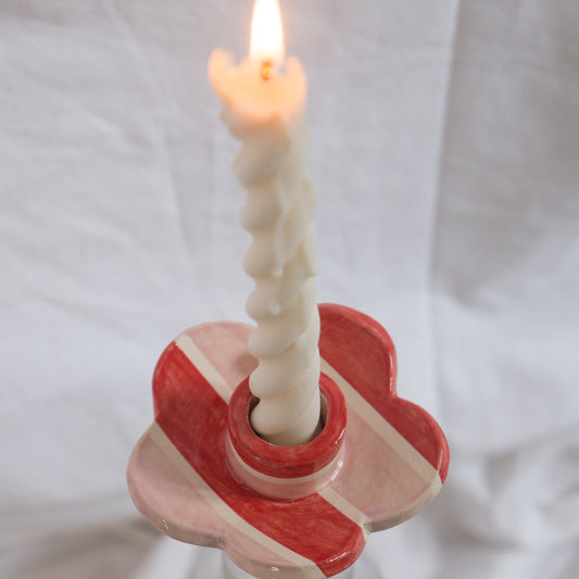 Ceramic candle holder with a lit candle on a white fabric background