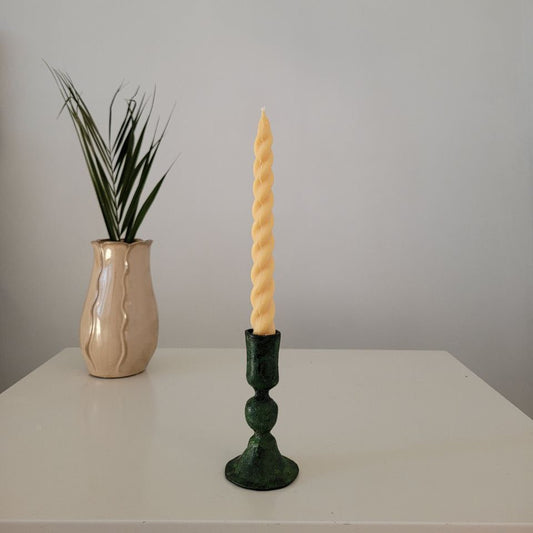 A collection of four Soie Soy Wax Twirl Taper Candles in various colors including green, gray, yellow, and white, displayed against a black background.