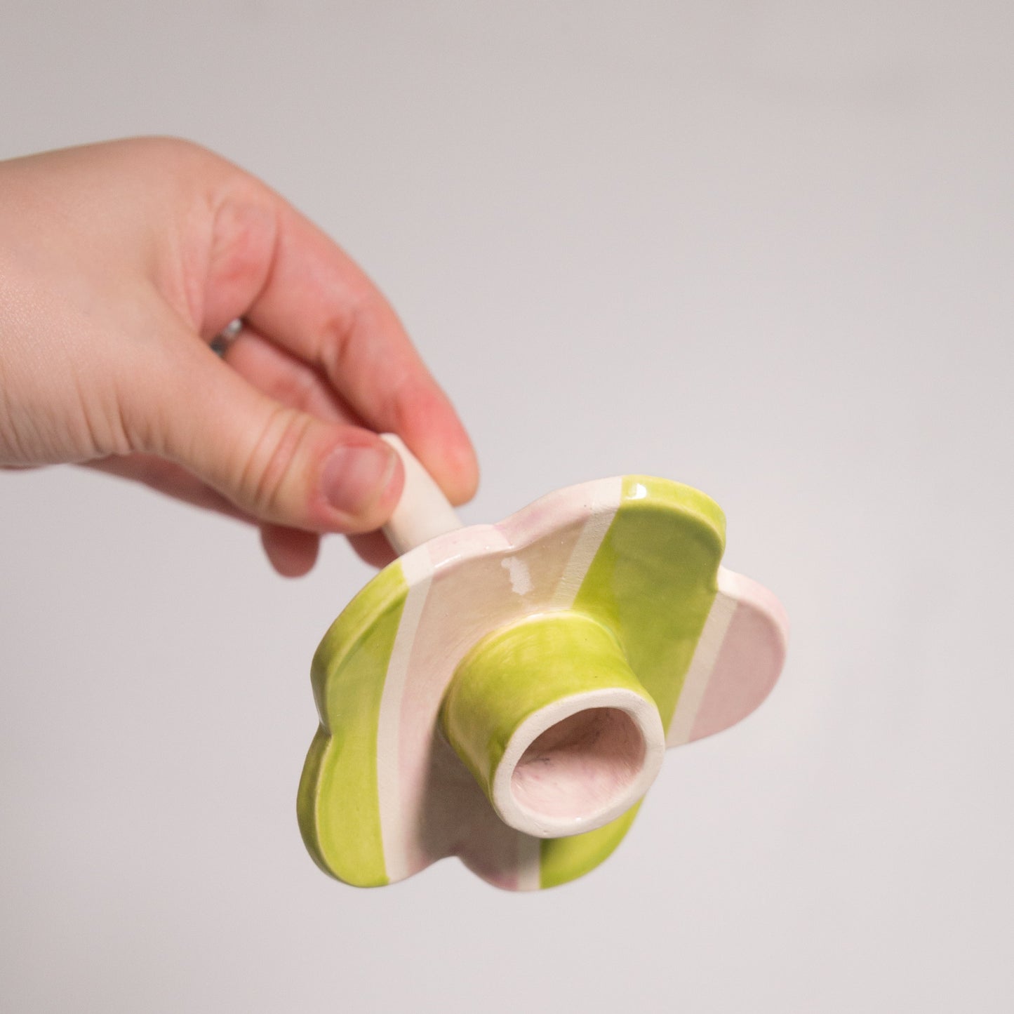 Hand holding a green and pink ceramic flower-shaped object against a plain background