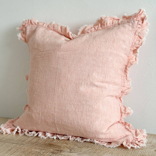 Ellenvale Ruffled Edge Linen Cushion in Washed Pink displayed on a bench against a white wall.
