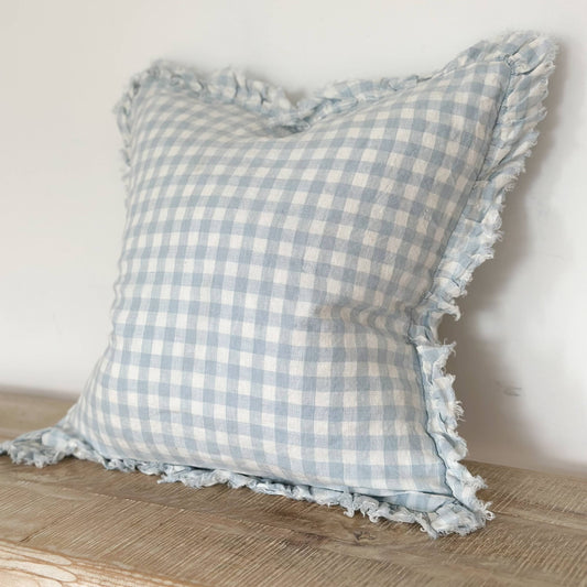 Ellenvale Ruffled Linen Cushion with ruffled edge in Blue Gingham displayed on a bench against a white wall.