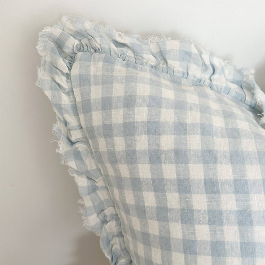 Ellenvale Ruffled Linen Cushion in Blue Gingham with a ruffle edge displayed on a bench against a white wall.