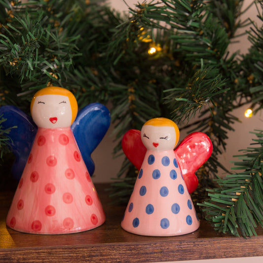 Two angel figurines with polka dot patterns in front of a Christmas tree.