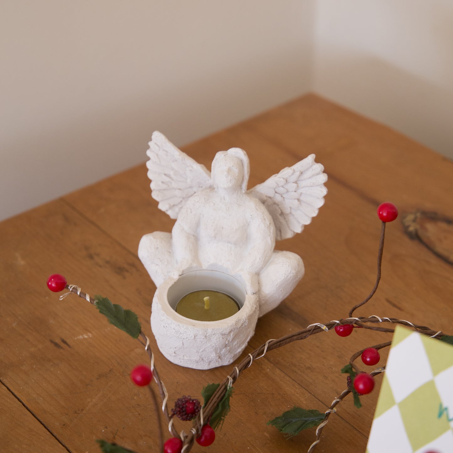 White angel-shaped candle holder with a lit candle on a wooden surface with decorative branches.