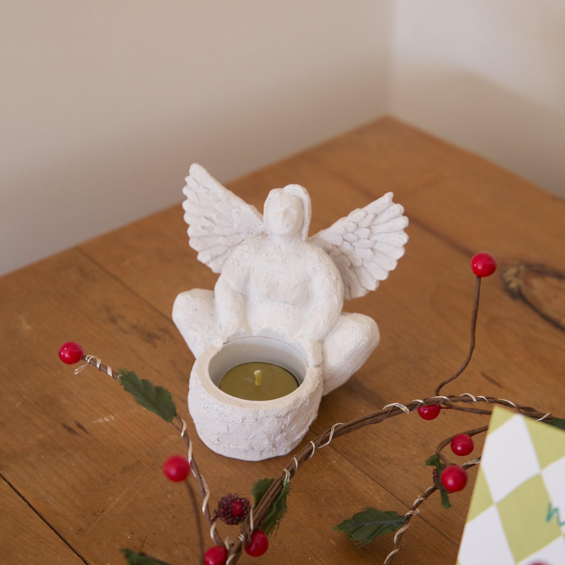 White angel-shaped candle holder with a lit candle on a wooden surface with decorative branches.