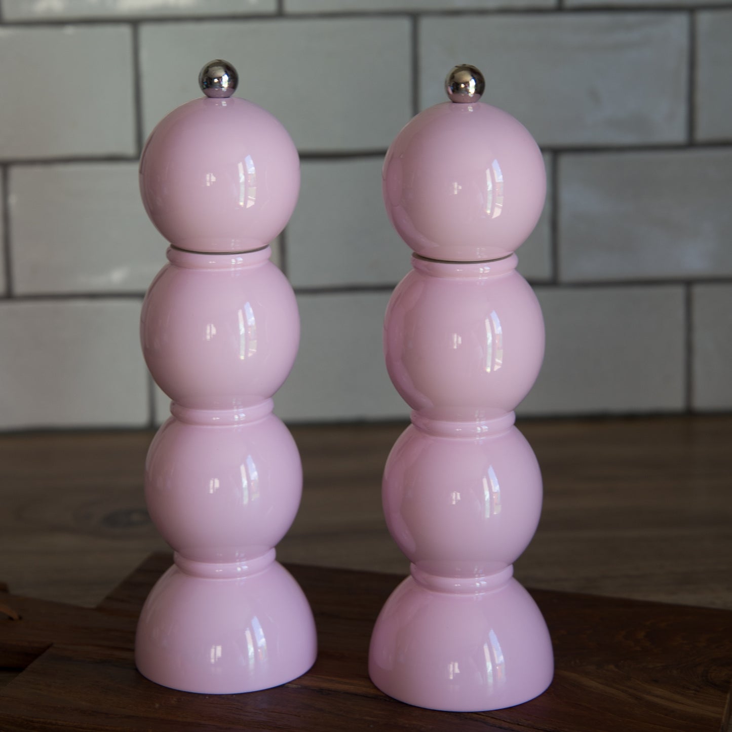 Two pink salt and pepper shakers on a wooden surface with a tiled wall background.