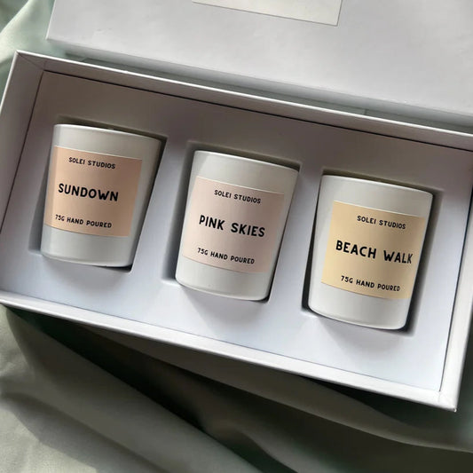 Three candles in a box with 'Solei Studios' branding on a soft fabric background.