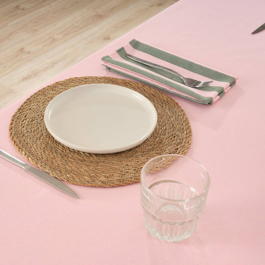 Pink and Green striped table serviettes, displayed on a pink tablecloth on the side of a woven placemat, cutlery, white plate and clear water glass.