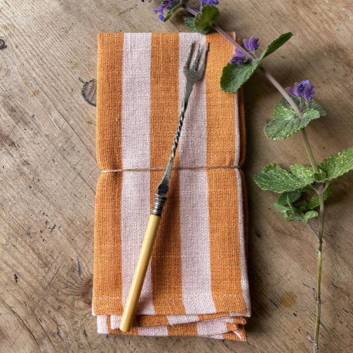 Folded orange and white striped napkin with a gold fork on a wooden surface with purple flowers.