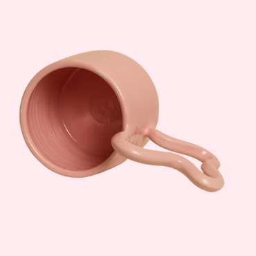 Pink ceramic mug with a unique handle design on a light pink background