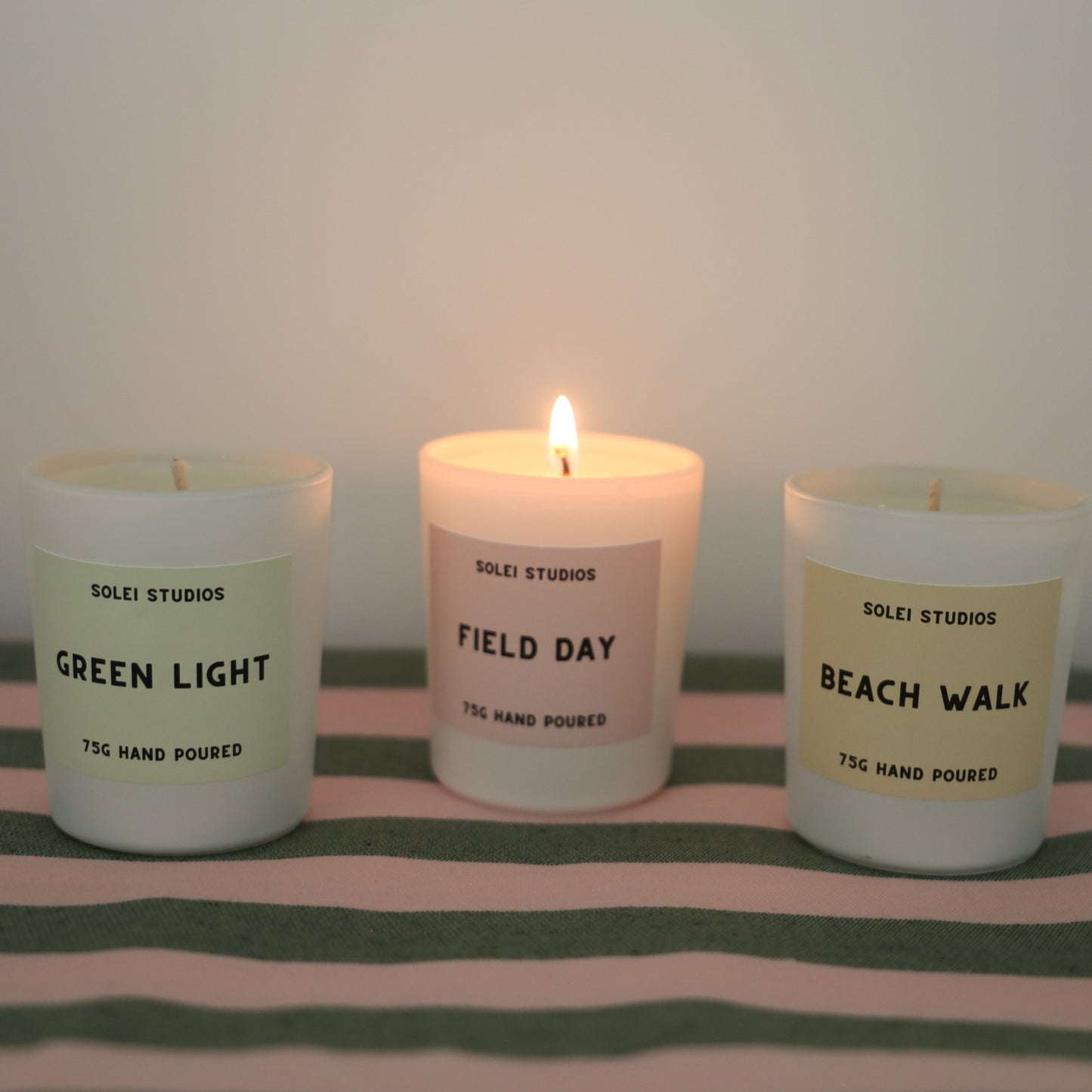 Solei Studios Mini Jar Candles in summer scents displayed with one burning and the others next to it. They are all displayed on a green and pink table cloth