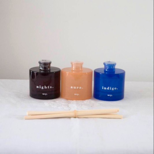 Three scented reed diffusers labeled 'nights', 'aura', and 'indigo' with wooden sticks on a light background.