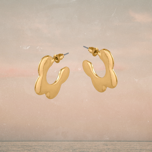 Gold hoop earrings on a light wooden surface with a soft background