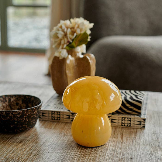 Yellow mushroom-shaped lamp on a wooden surface with a vase and flowers in the background