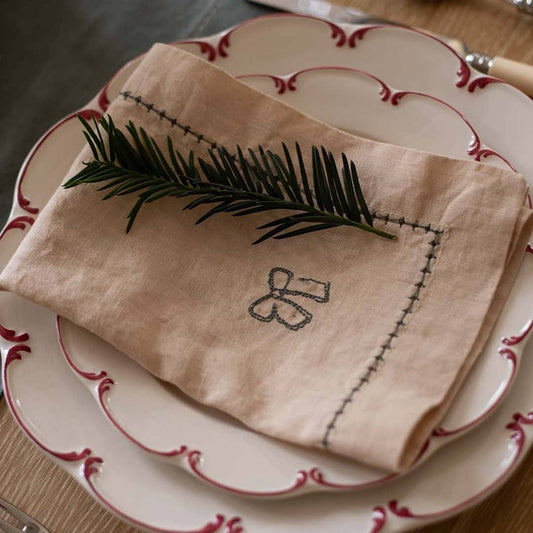 Folded beige napkin with embroidered design on a set of white plates with red trim.