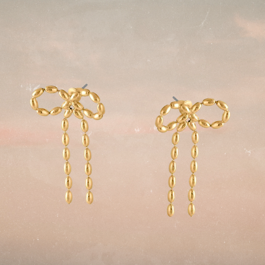 Gold bow-shaped earrings with dangling beads on a neutral background