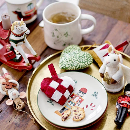 A collection of Christmas-themed paper mache ornaments including a heart, a Christmas tree, and other festive figures, displayed on a table with a cup of tea and decorative cookies.