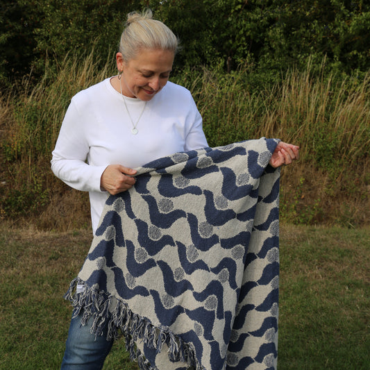 Person holding a patterned blanket outdoors with trees in the background