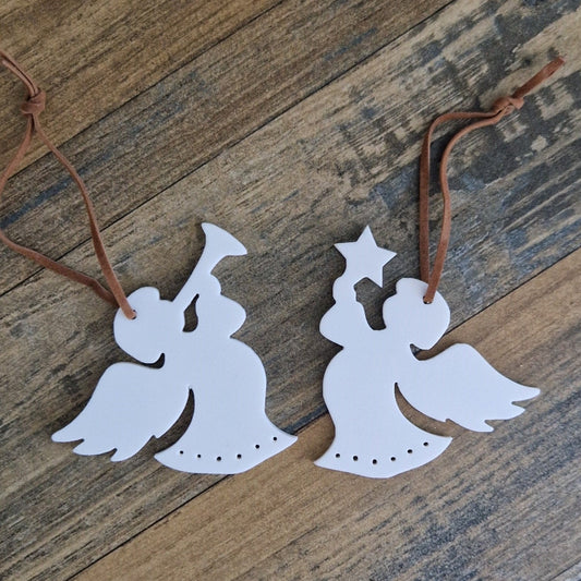 Two white stoneware angel ornaments with star details, suspended by brown strings against a wooden background.