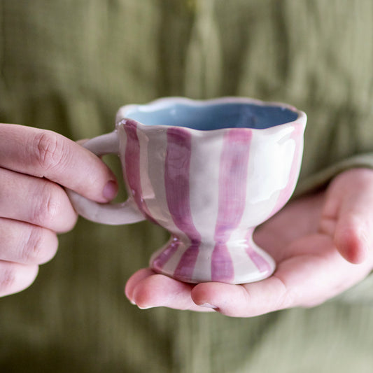 Person holding a small ceramic cup with purple and white stripes.