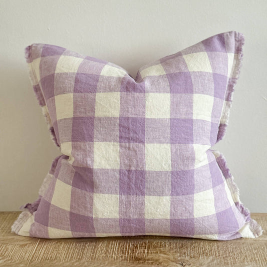 Purple and white checkered pillow on a wooden surface with a neutral background