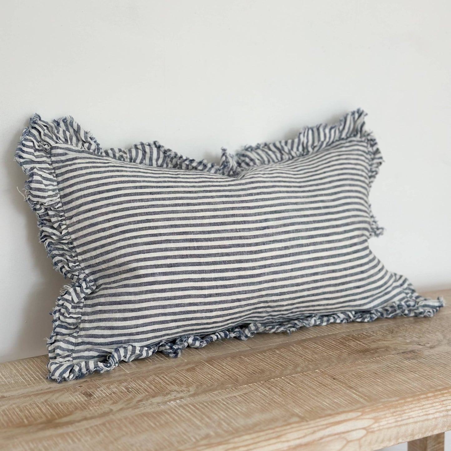Striped pillow with ruffled edges on a wooden surface against a white background