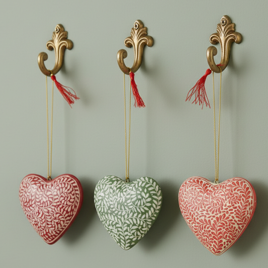 A set of three papier-mâché heart-shaped Christmas ornaments in red, green, and pink colors with intricate patterns and hanging hooks.