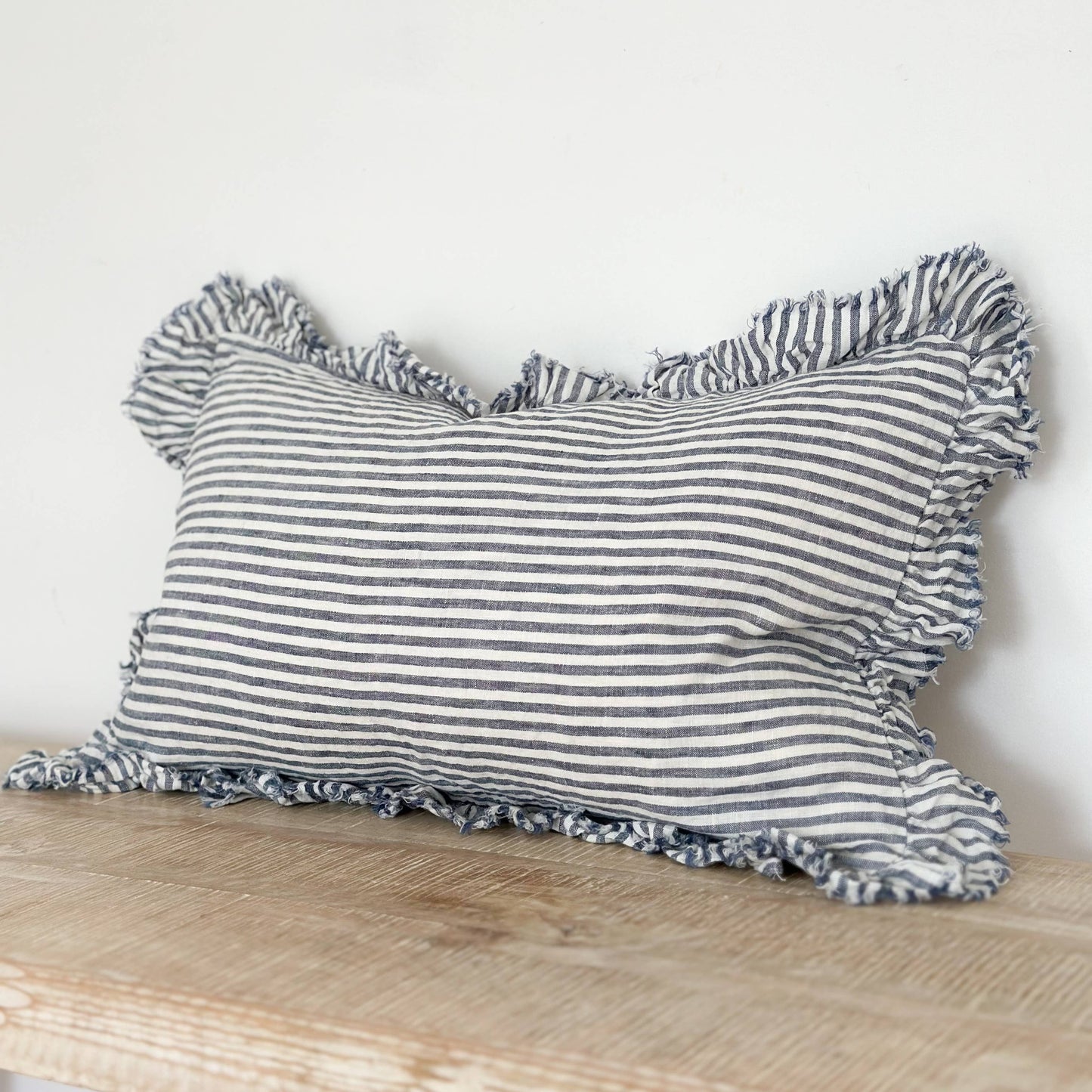 Striped pillow with ruffled edges on a wooden surface against a white background