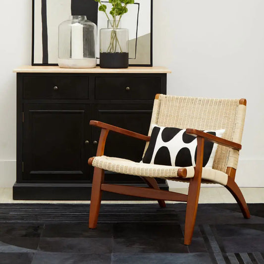 Wooden armchair with cowhide pattern and woven backrest in a room with a black cabinet and mirror.