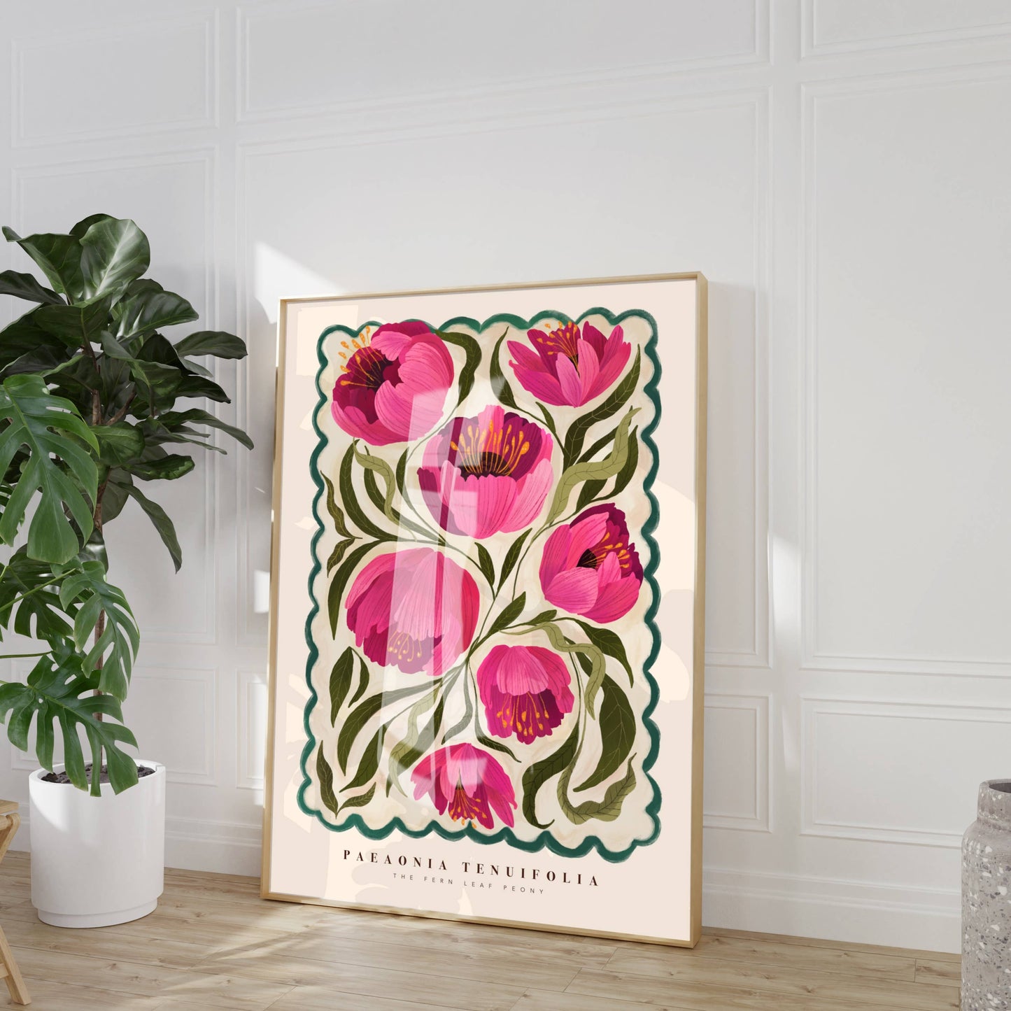 Framed floral artwork with pink flowers in a room with a plant and vase.