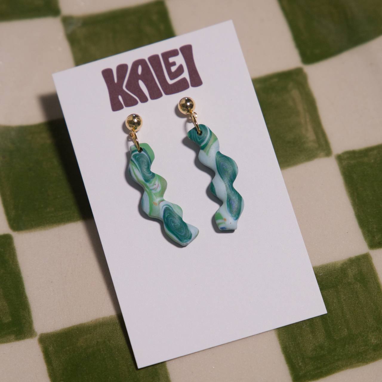Green marbled earrings on a white card with 'KALEI' branding, against a green and beige checkered background.
