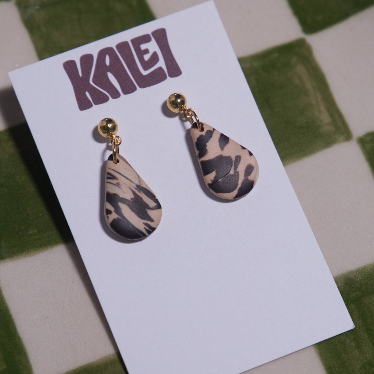 Teardrop-shaped earrings on a 'KALEI' branded card against a green and white checkered background.