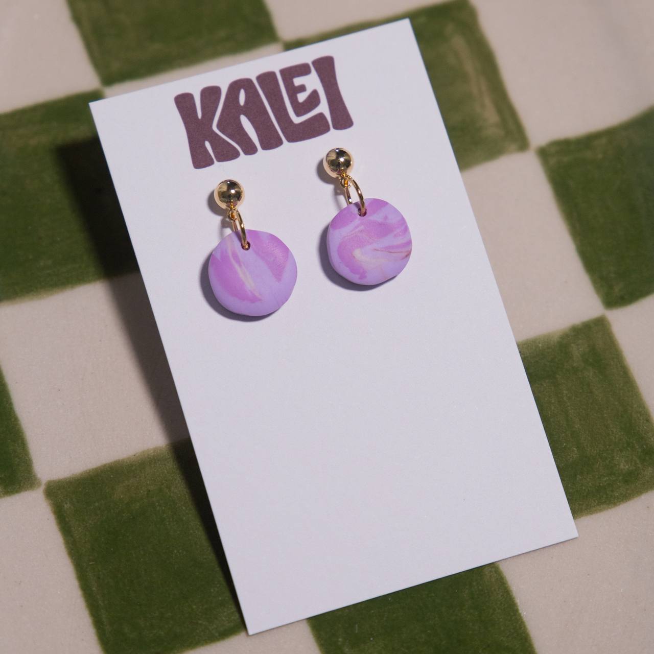 Purple marbled earrings on a 'KALEI' branded card against a checkered background