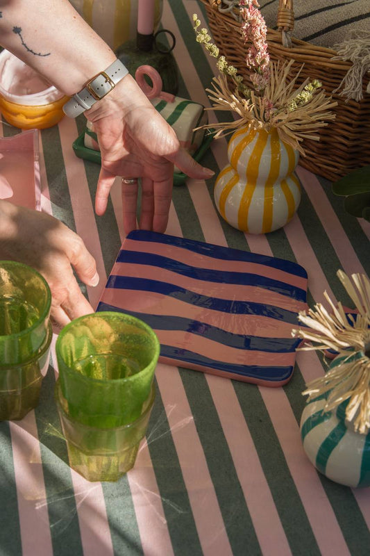 Pink and Blue wiggle striped ceramic tray displayed on an outside table scene with a model placing the tray down
