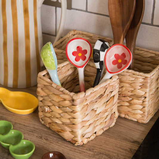 Decorative spoons with floral designs in a woven basket on a kitchen counter.
