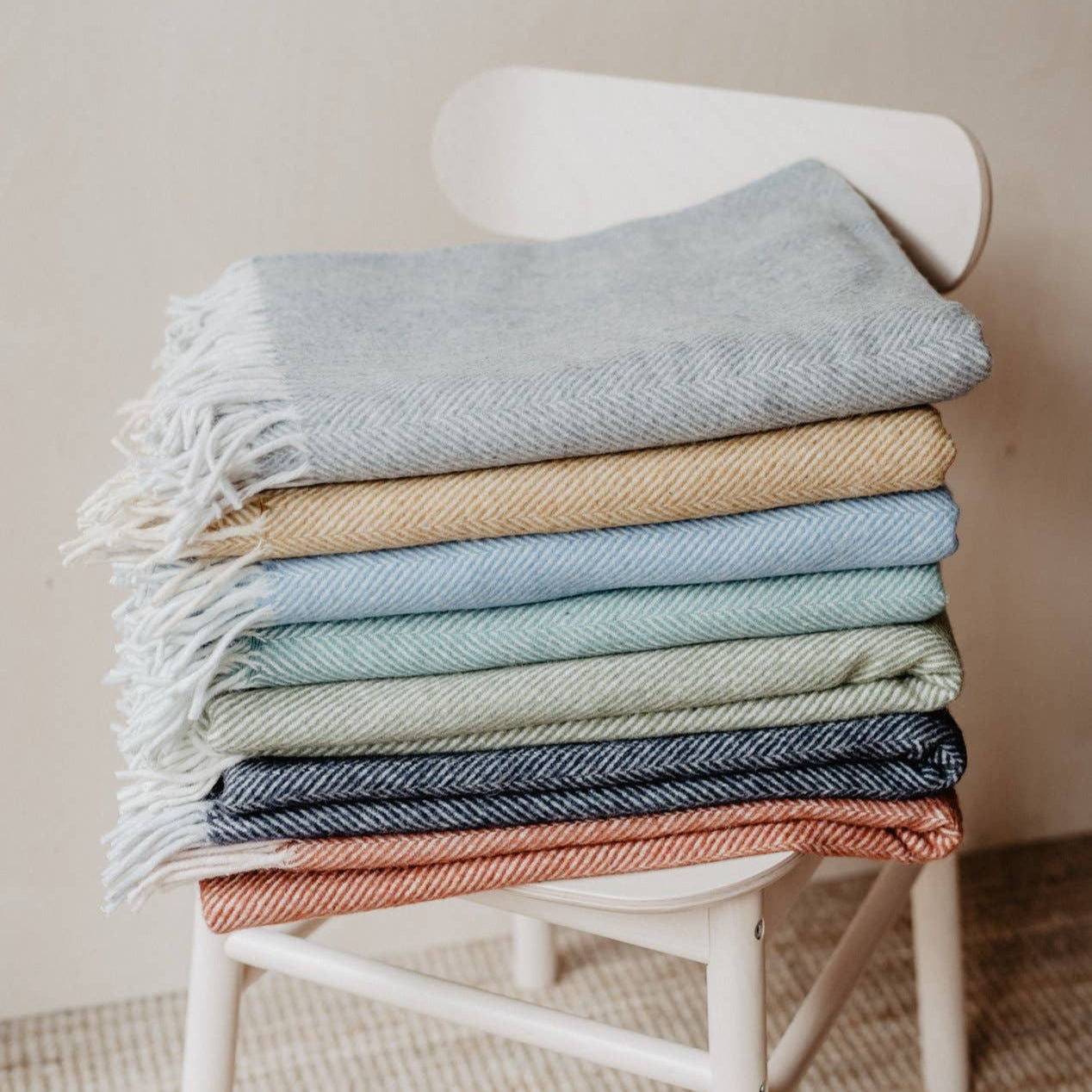 TBCo knee blankets in various colours folded and displayed on a chair.