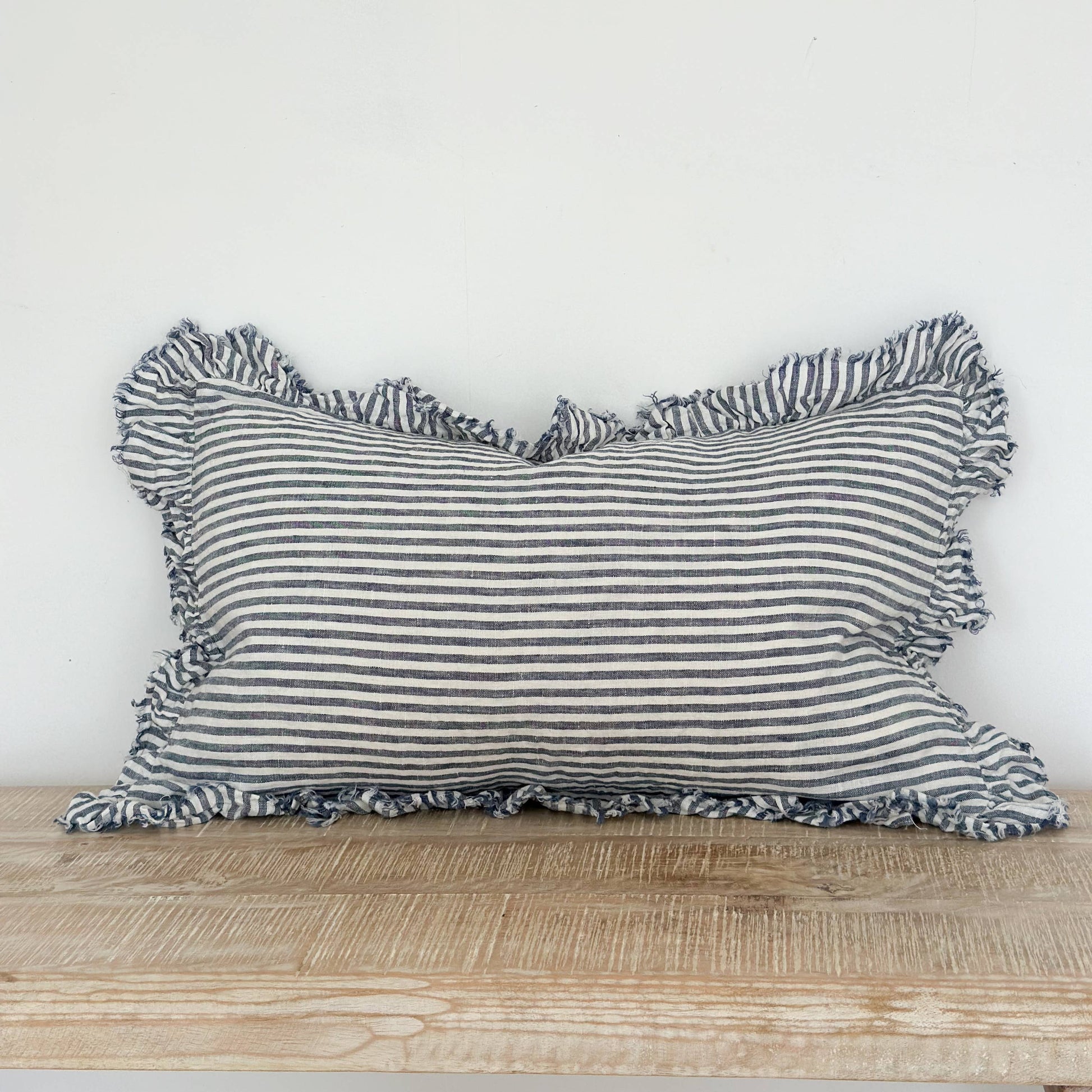 Striped pillow with ruffled edges on a wooden surface against a white background