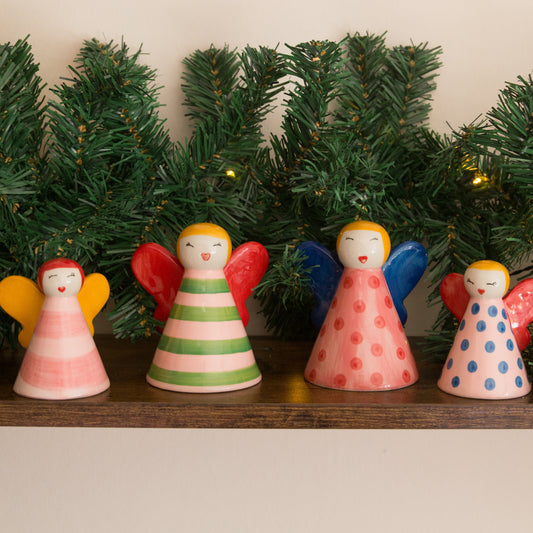 Colorful angel figurines on a shelf with Christmas tree decorations in the background