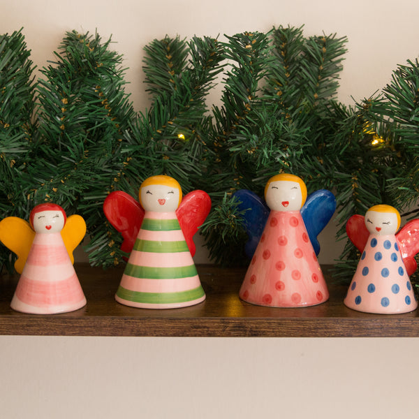 Colorful angel figurines on a shelf with Christmas tree decorations in the background