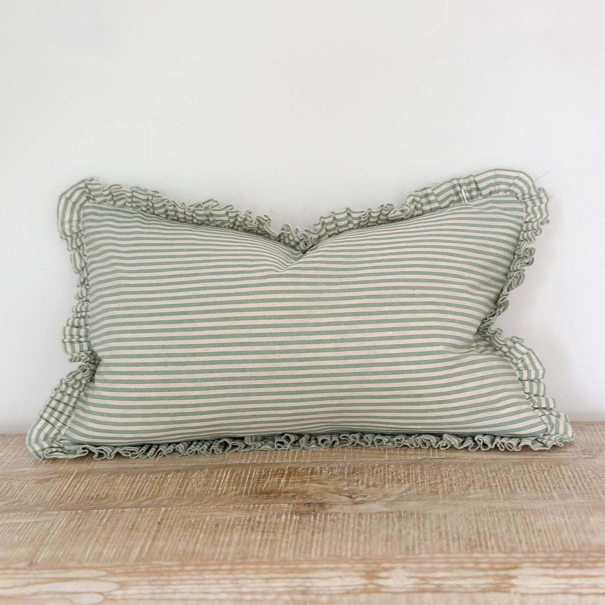 Green striped pillow with ruffled edge on a wooden surface against a white wall