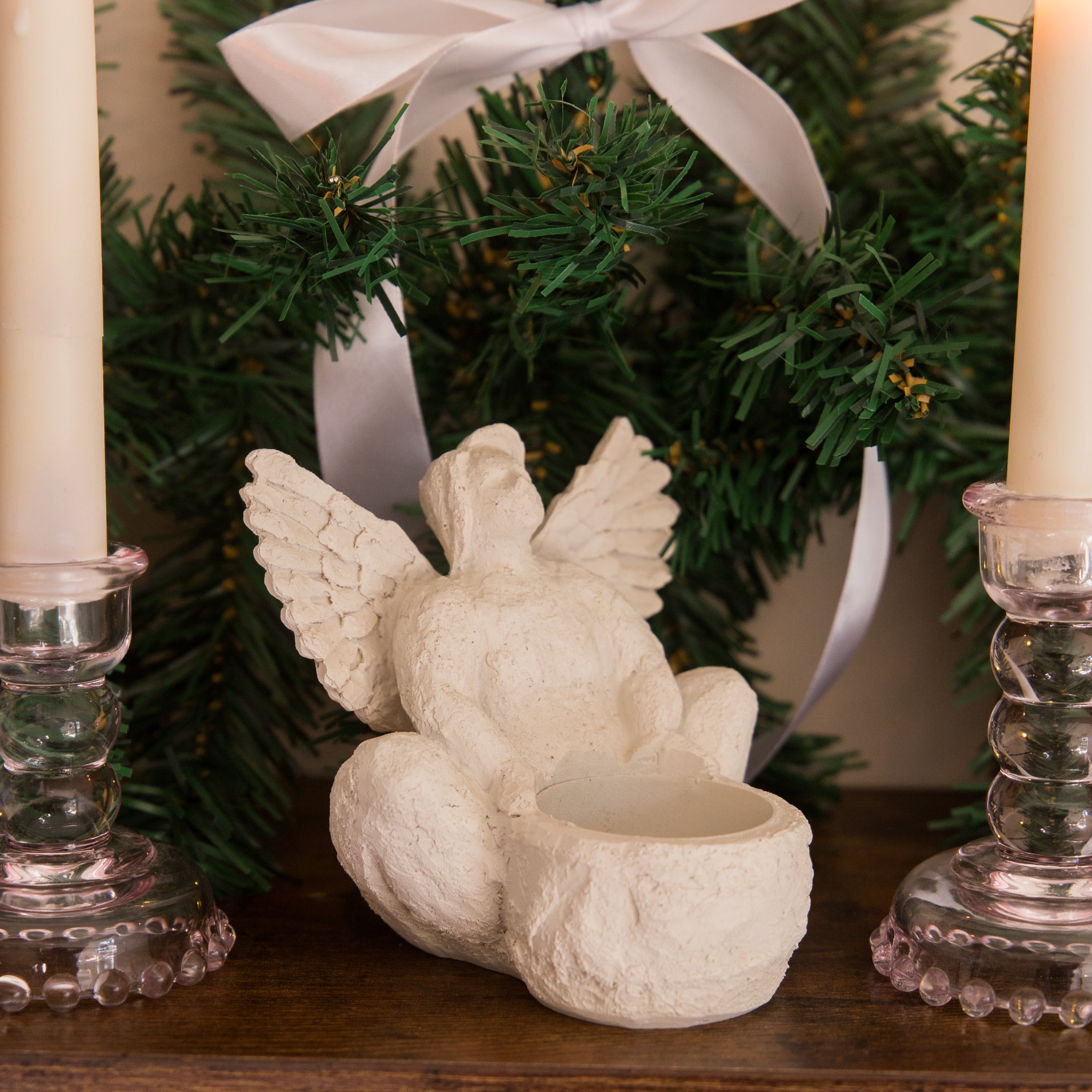 Decorative angel figurine with a candle holder in front of a Christmas tree.
