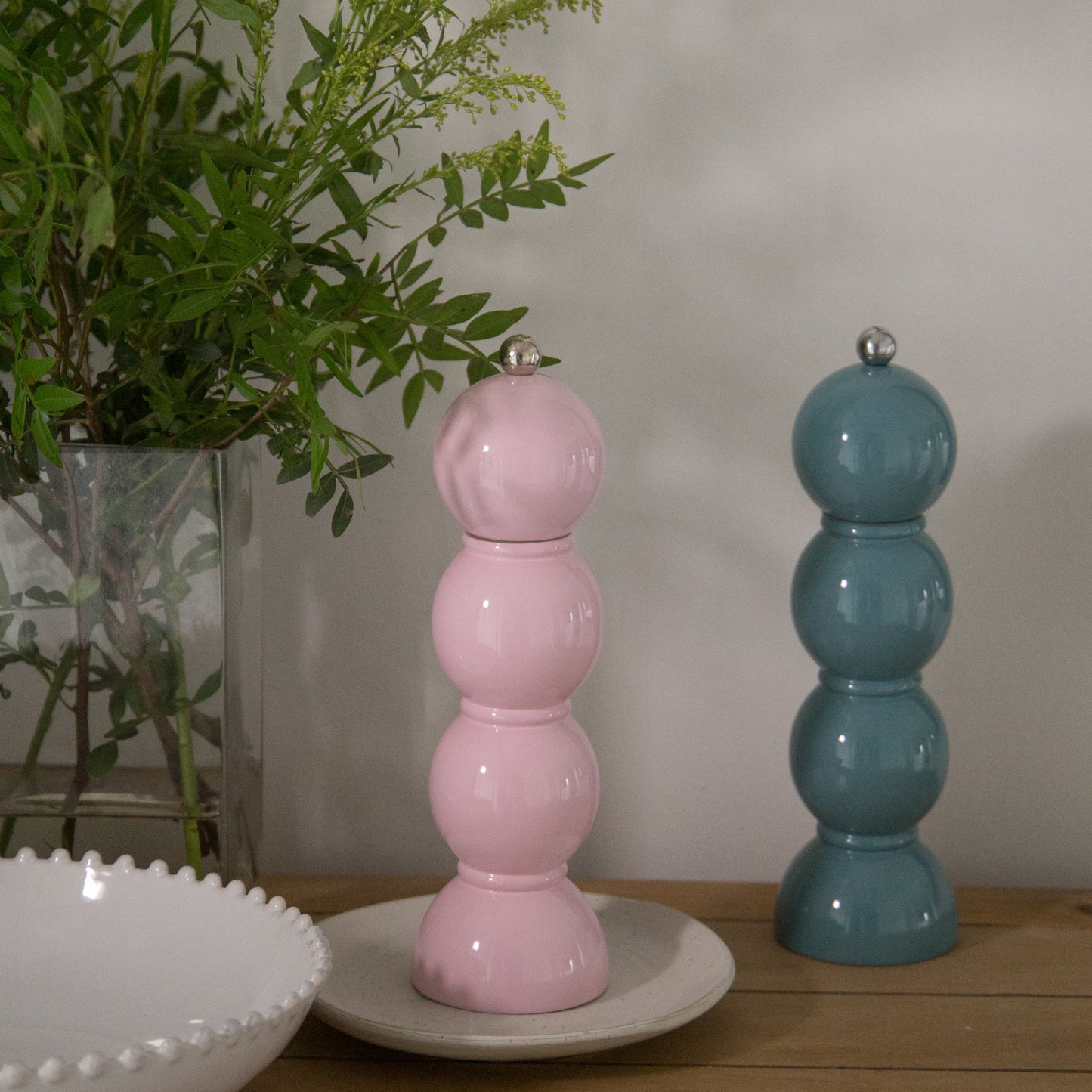 Pink and blue ceramic salt and pepper shakers on a wooden surface with a plant in the background.
