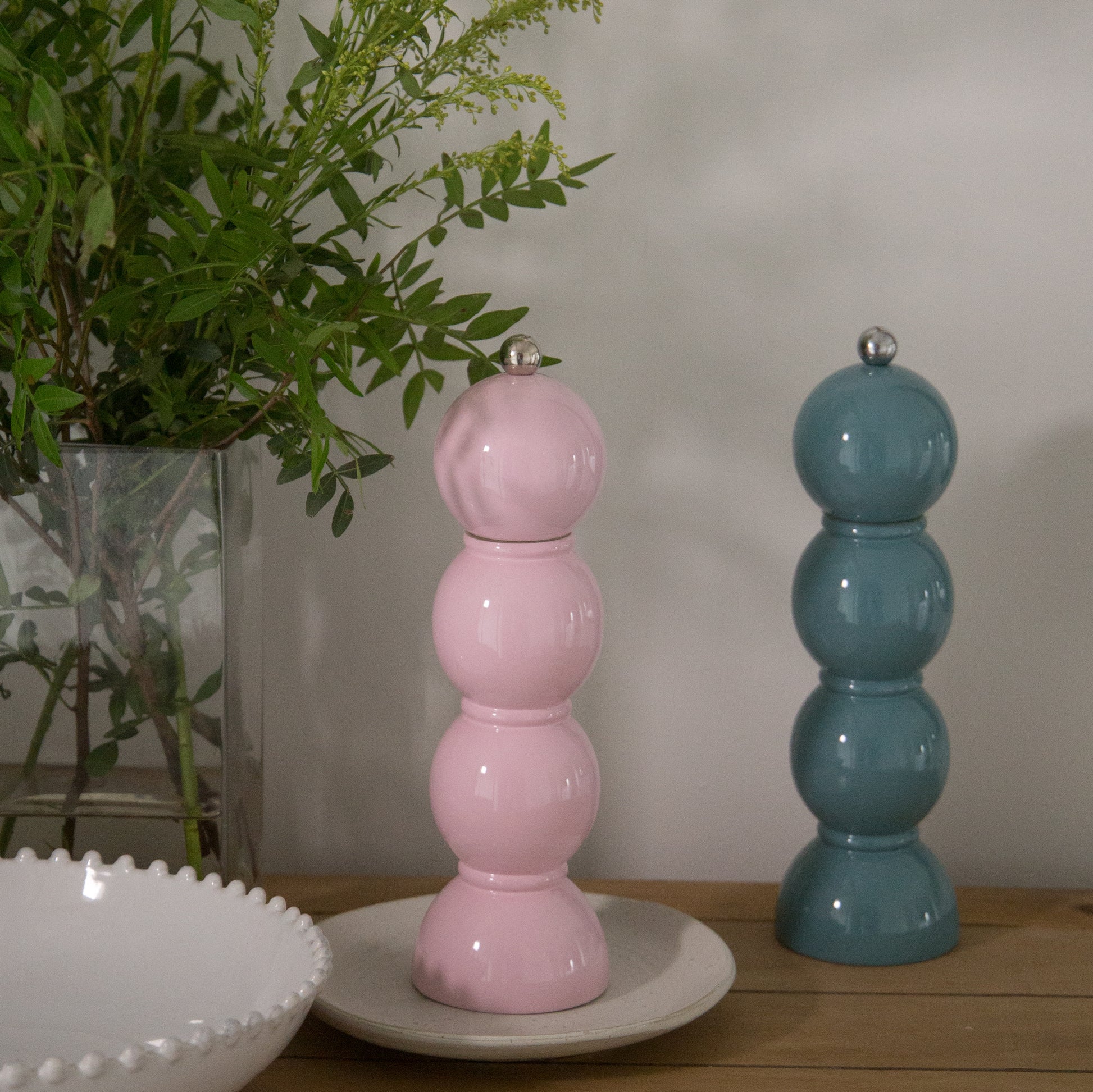 Pink and blue ceramic salt and pepper shakers on a wooden surface with a plant in the background.